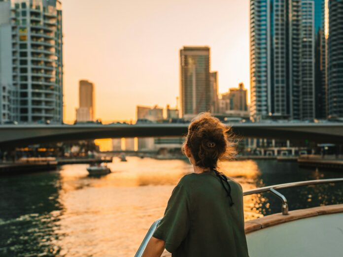 Photo by Dawid Tkocz Woman on boat overlooking city skyline at sunset