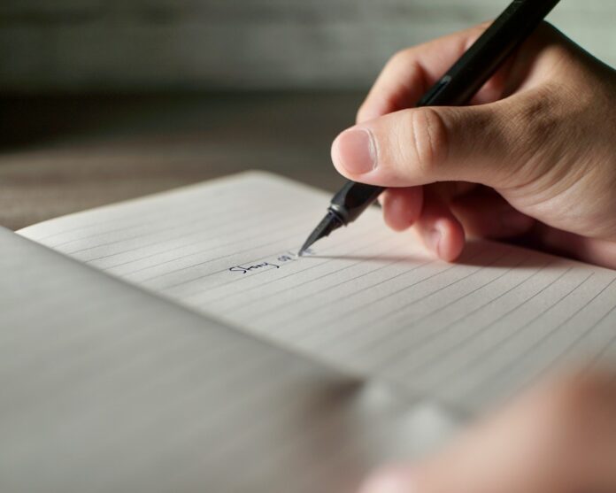 Photo by Khoiru Abdan a person writing on a piece of paper with a pen